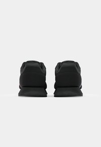 Schwarze Sportschuhe mit einem glatten Textil-Obermaterial, gepolstertem Absatz und Gummisohle mit einem Zickzackmuster, die ein elegantes Design präsentieren.