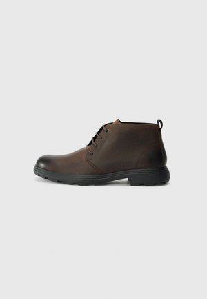 Botas de cuero marrón hasta el tobillo con punta redondeada, suela de goma negra y un diseño de cordones minimalista. Acabado texturizado con una tira en el talón.