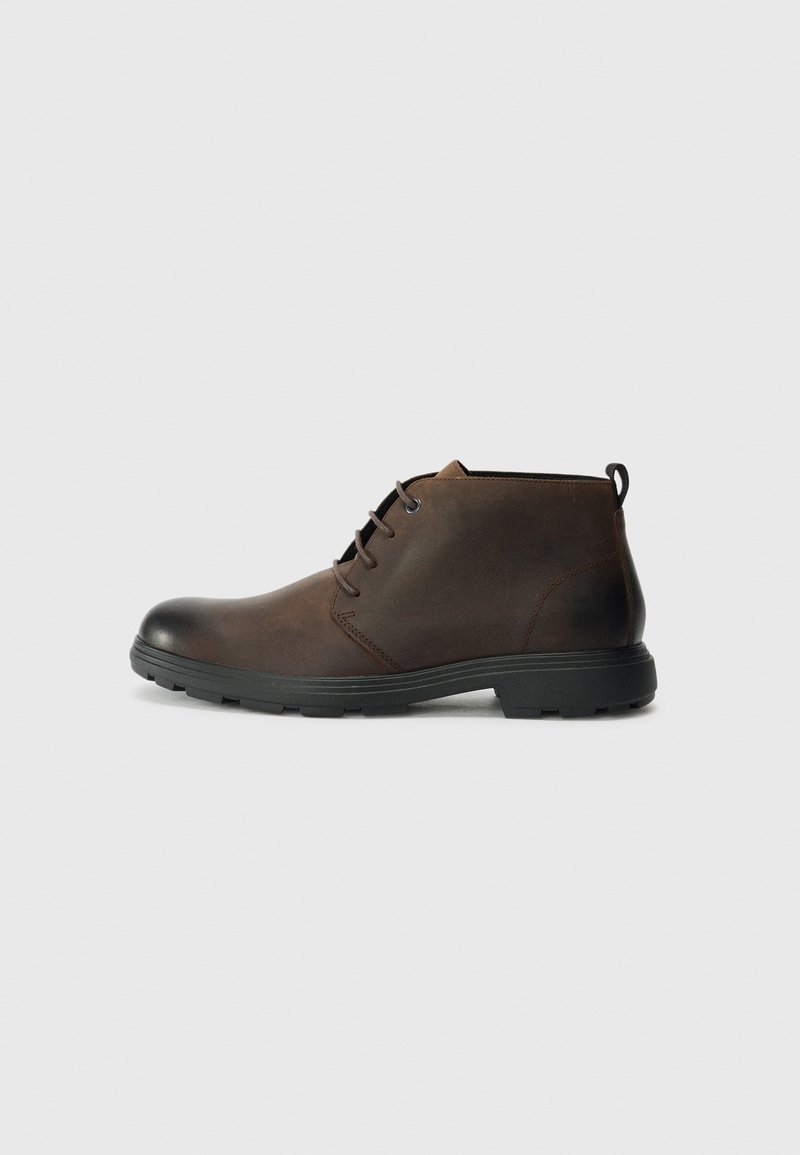 Botine din piele maro, cu vârf rotund, talpă din cauciuc negru și un design minimalist cu șireturi. Finisaj texturat cu un tab de prindere la călcâi.