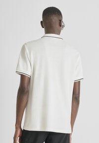 Chemise polo blanche avec des finitions noires sur le col et les manches, fabriquée en tissu lisse, dotée d'une coupe classique et de manches courtes.