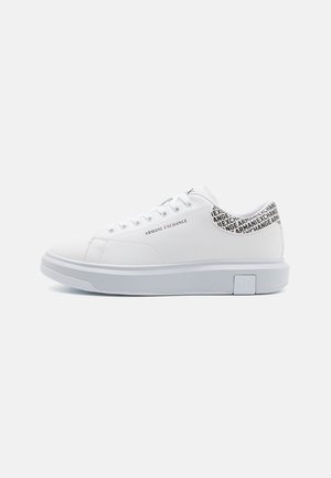 Zapatillas blancas con parte superior de cuero sintético suave, punta redonda y suela de goma blanca plana. La parte trasera presenta un patrón de texto negro con "Armani Exchange."
