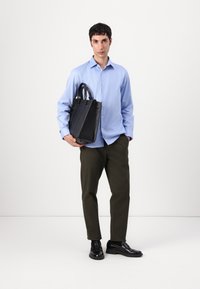 Zila pogca krekls, tumši zaļi bikses, melnas ādas kurpes; vīrietis tur melnu ādas rokassomu ar divām rokturiem. Minimalistisks dizains.