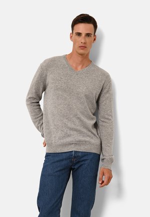 Grijze wolmix trui met een V-hals, geribde manchetten en zoom, gecombineerd met donkerblauwe denim jeans, staande tegen een effen achtergrond.