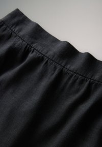 Sort linnednederdel med en elastisk taljebånd, der er samlet. Stoffet virker letvægtigt med en glat tekstur, hvilket skaber en subtil drapering.