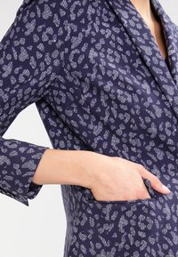 Námorný látkový blejzr s bílým abstraktním leopardi vzorem, jednou kapsou a klopovým límcem, s hladkým, texturovaným povrchem.