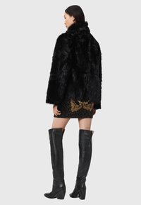 Czarny sztuczny futrzany płaszcz z wysokim kołnierzem, noszony na wzorzystą mini spódnicę, w połączeniu z czarnymi skórzanymi kozakami do kolan.