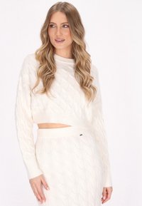 Witte gebreide cropped trui met kabelpatroon, lange mouwen en een ronde halslijn, gecombineerd met een bijpassende high-waisted rok.