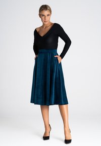 Czarna bluzka z długim rękawem w kształcie litery V, połączona z turkusową, welurową spódnicą do kolan, posiadającą dopasowaną talię i boczne kieszenie.