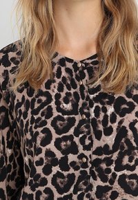 Bluse mit Leopardenmuster in Beige und Schwarz, mit rundem Halsausschnitt, Knopfverschluss und einem weichen, leichten Stoff.