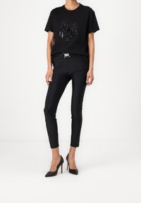 Black short-sleeve t-shirt with sequin design, paired with black fitted pants and black high-heeled shoes, presenting a sleek silhouette.