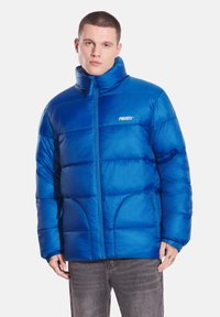 Niebieska kurtka puchowa z wysokim kołnierzem, zamkiem błyskawicznym i widocznym przeszyciem. Posiada elastyczne mankiety i logo na klatce piersiowej.