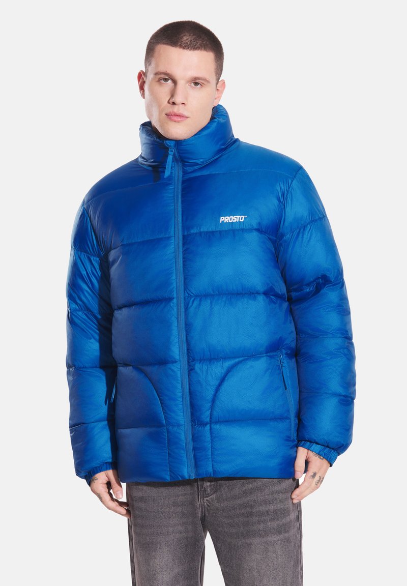 Niebieska kurtka puchowa z wysokim kołnierzem, zamkiem błyskawicznym i widocznym przeszyciem. Posiada elastyczne mankiety i logo na klatce piersiowej.