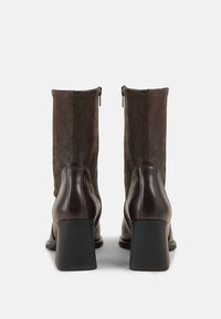 Brown leather ankle boots with a high block heel, featuring a smooth finish and a zip closure at the back. Suede upper adds texture.