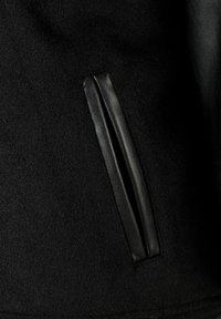 Giacca nera in lana con una elegante tasca in pelle inserita, dalla texture morbida e dettagli sottili, che enfatizzano gli elementi di design moderni.