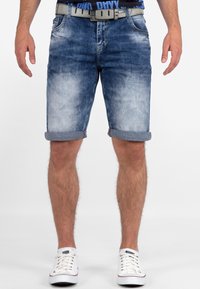 Lichtblauwe denim shorts met een vervaagde afwerking, opgerolde taille, vijf zakken en een grijze riem. Gepaarde met witte sneakers.