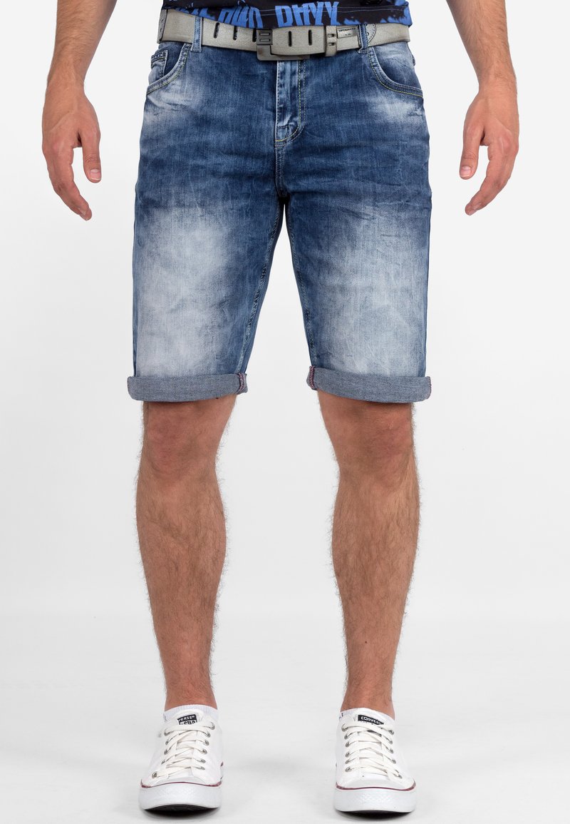 Shorts in denim di colore azzurro chiaro con una finitura sbiadita, orli arrotolati, cinque tasche e una cintura grigia. Abbinati a sneakers bianche.