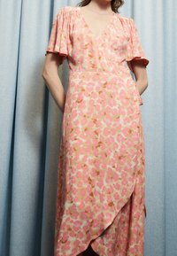 Vestido envolvente floral rosa con mangas cortas y con volantes, que presenta un escote en forma de V y un dobladillo asimétrico. Tela ligera con una textura suave.