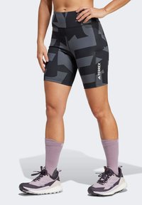 Čierne a šedé vzorované športové šortky s vysokým pásom, s logom "Terrex" na boku, skombinované s fialovými ponožkami a topánkami.