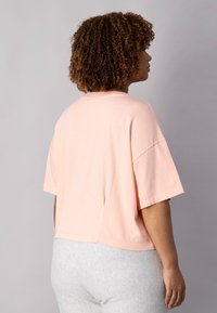 Lys pink cropped t-shirt lavet af bomuld, med korte ærmer, rund halsudskæring og afslappet pasform. Glat tekstur og enkelt design.