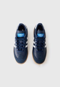 Námornícky modré tenisky Adidas Samba s bielymi pruhmi, vyrobené z kože a semišu, s okrúhlou špičkou a gumovou podrážkou. Disponujú šnurovacím dizajnom.