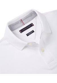 Polo shirt blanc en tissu texturé, col standard, deux boutons et col intérieur rayé. Présente le logo Tommy Hilfiger.