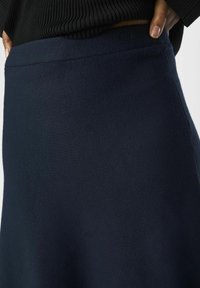 Falda azul marino fabricada con un tejido suave y de textura lisa. Presenta una cintura ceñida y una silueta acampanada.
