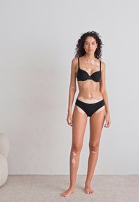Black bra and bikini set featuring a simple design with adjustable straps, seamless cups, and a classic low-rise fit on a model against a neutral background.