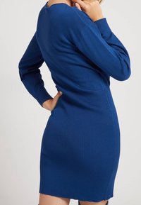 Robe tricotée bleue à côtes, avec des manches longues, au design ajusté et dos plongeant. Le tissu texturé met en valeur la silhouette près du corps.