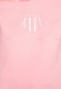 Felpa in cotone rosa con logo scudetto ricamato e strisce verticali, e testo che recita "GANT AMERICAN SPORTSWEAR."