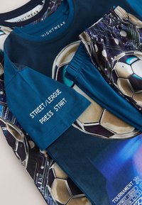 Blåt og sort sovetøj med fodboldtema med grafik af fodbold og teksten "STREET/LEAGUE PRESS START" på ærmet.