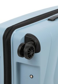 Světle modrý kufr s tvrdou skořepinou má texturovaný povrch, černý zip a dvě černé kola v rozích pro snadnou manipulaci.