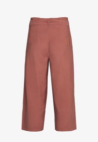 Pantalons évasés couleur rouille en tissu léger, avec une taille haute, des plis avant et une texture lisse.