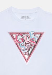 Weißes T-Shirt aus Bio-Baumwolle mit einem großen, bunten dreieckigen Grafikdesign und Paillettenbuchstaben in Pink, Blau und Schwarz.