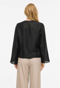 Sort, teksturert langermet topp med rund hals. Baksiden har en sentral søm. Kombinert med beige, vide bukser.