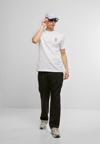 White T-shirt with a small graphic, black trousers, light blue cap, sunglasses, and gray sneakers. Casual outfit with modern design elements.