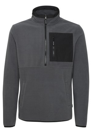 Pull-over en molleton gris avec un col montant, fermeture éclair sur le devant et une poche poitrine noire. Comprend des poches latérales et des accents noirs contrastants.