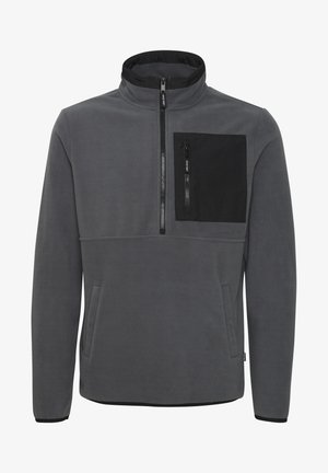 Grå fleece-genser med høy krage, glidelås foran og en svart brystlomme. Har sidelommer og kontrasterende svarte detaljer.