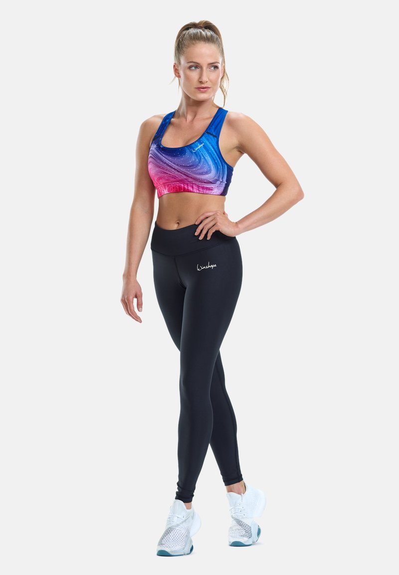 Sports bra in blue and pink gradient with a swirling pattern, paired with black leggings. The leggings feature a logo at the hip.