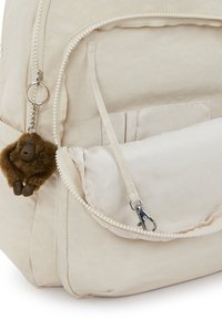 Hellbeiger Rucksack aus weichem Stoff, mit einer Reißverschlusstasche vorne, einem plüschigen Affen-Schlüsselanhänger und glatten Texturen.