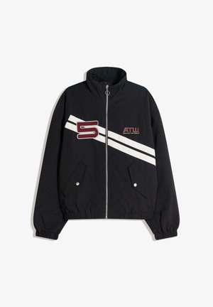Musta vetoketjullinen takki, jossa joustavat hihansuut, kaksi etutaskua, vinoja valkoisia raitoja ja etupuolella punainen "S"- ja "ATW"-logo.