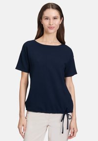 Granatowa bluzka z krótkim rękawem, wykonana z teksturowanej tkaniny, z okrągłym dekoltem i regulowanym wiązaniem w okolicy bioder dla dopasowanego wyglądu.