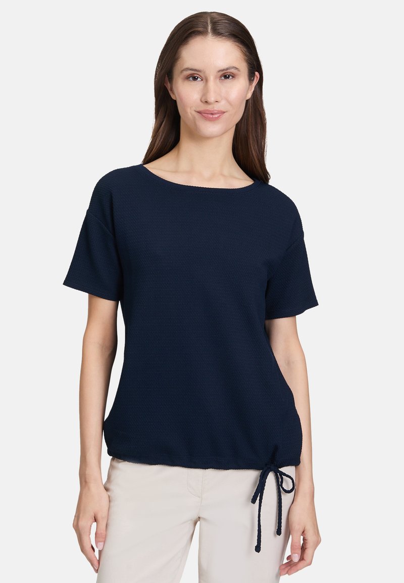 Granatowa bluzka z krótkim rękawem, wykonana z teksturowanej tkaniny, z okrągłym dekoltem i regulowanym wiązaniem w okolicy bioder dla dopasowanego wyglądu.