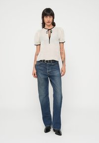 Vit texturerad blus med svarta kanter och knyt runt halsen, kombinerad med ljusblå jeans med raka ben och svarta skor med spetsigt toe.