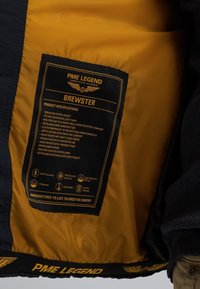 Granatowa nylonowa kurtka puchowa z żółtym wnętrzem. Wyposażona w metkę produktową, elastyczne mankiety, kieszenie wewnętrzne i zewnętrzne oraz odpinany kaptur.