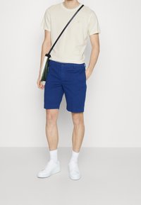 Blå shorts med en glat overflade, en knaplukning og en foldet kant. Parret med en kremfarvet t-shirt og hvide sneakers, med en crossbody taske.