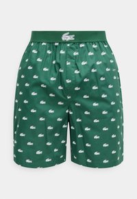 Boxers vert foncé avec une ceinture élastique, ornés de logos crocodile blancs imprimés partout et d'un logo crocodile plus grand sur la ceinture.