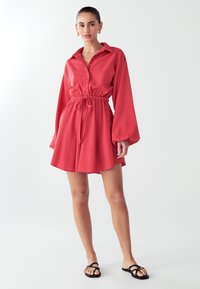 Rotes Hemdkleid mit langen Ärmeln, kragenlosem Ausschnitt, Kordelzug in der Taille und ausgestelltem Rock. Glattes Material mit lockerer Passform.