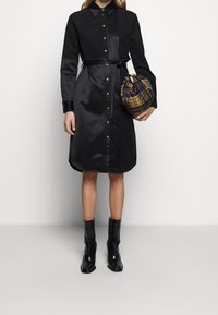 Svart satin skjortklänning med knäppning fram, långa ärmar och ett matchande bälte. Kombinerad med en rutmönstrad dragsko-väska och svarta ankelstövlar.