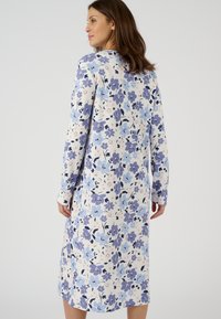 Vestido de estampado floral con flores azules y moradas sobre un fondo claro, mangas largas y corte a la altura de la rodilla con textura acanalada.