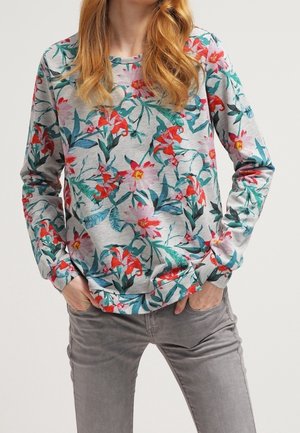 Felpa floreale grigia chiara con motivi di fiori rossi e rosa, maniche lunghe, scollatura rotonda e tessuto morbido e testurizzato. Abbinata a pantaloni grigi.